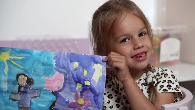 Talented Creative Child Girl Female Artist Draws Ranbow Mother summer on Paper, Child showing her work.Creates Colorful, Kid Drawing on table at Home. Painter Creating Abstract Modern Art. Childhood