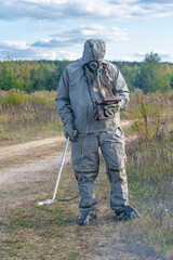 A military man in chemical protection and a gas mask measures the radiation level with a dosimeter in nature, smoke from a fire. Concept: radiation leakage, radioactive hazard.