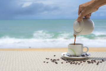 Relaxing vacation Maldives vacation. Hands  pouring coffee from pot into cup. near the Indian ocean. Spa relaxing time at the beach with white sand. Hot beverage near the sea...