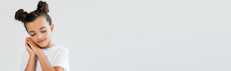 Fototapeta premium sleepy girl with folded hands and glitter stars on cheeks posing isolated on grey, banner.