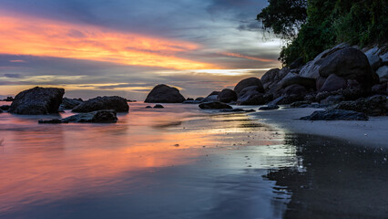 Scenic saturated seascape with stones in sea water on shore at beautiful colorful sunset on beach. Long exposure. Phuket, Thailand