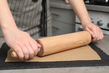 Woman rolling dough with wooden pin at table in kitchen, closeup