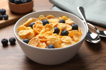 Bowl of tasty crispy corn flakes with milk and blueberries on wooden table, closeup