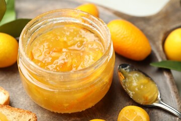 Delicious kumquat jam in jar and fresh fruits on wooden board, closeup