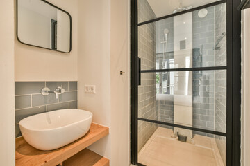 Tiled shower cabin with glass door located near sink and mirror in light restroom in contemporary...