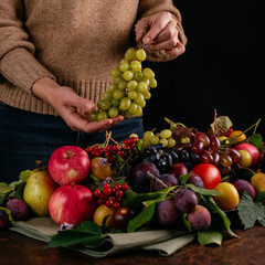 a girl holds green grapes against the background of autumn fruit