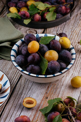 fresh ripe plums in a light ceramic plate on a wooden background