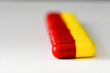 Close up view of a row of unmarked red and yellow gelatin capsules containing drugs on a plain white background. No people.