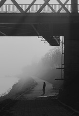 Silhouette of young woman walking under river bridge on a misty winter day