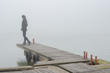 Young woman standing on the river dock in winter mist