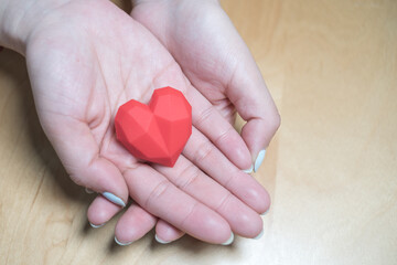 Fototapeta premium Adult holding red heart in hands over a wooden table. Family relationships,health care,cardiology concept,heart health care concept