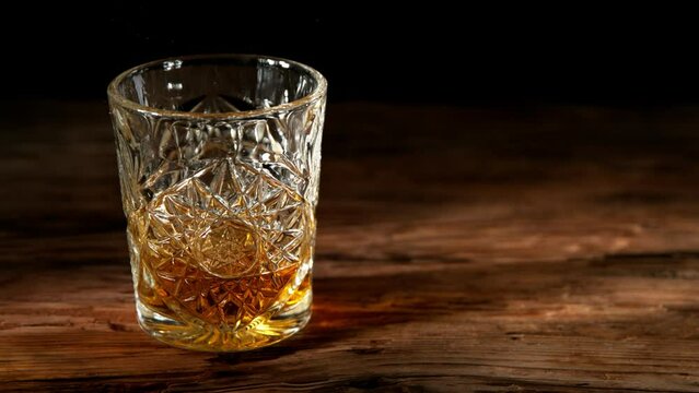 Super slow motion of falling ice cube into whisky drink. Placed on old wooden table. Filmed on high speed cinema camera, 1000fps. Speed ramp effect.