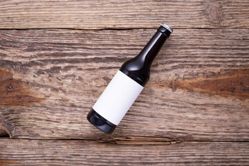 Beer bottle lies on wooden background with hop cones, close up. White label mock up