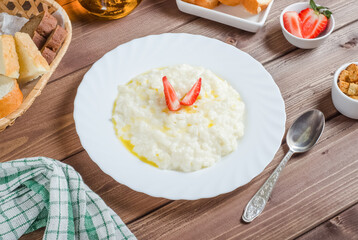 Delicious rice milk porridge with butter and strawberries in a white plate on a wooden background.