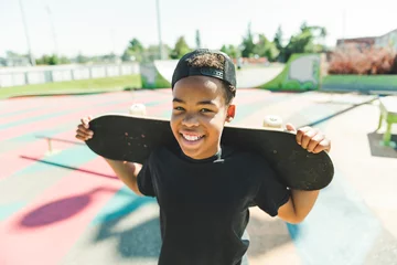 Foto op Plexiglas Afro-American boy with black t-shirt posing with his skateboard with the sky in the background © Louis-Photo