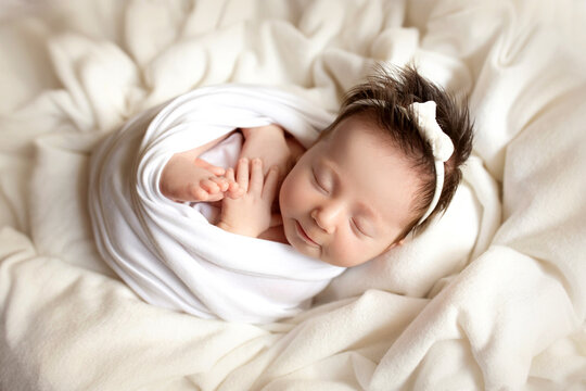 Top view of a newborn baby girl sleeping in a white cocoon on a white bed. Beautiful portrait of a little girl 7 days, one week. Macro studio professional photography.