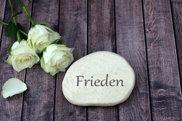 Das Wort Frieden auf einem Stein mit weissen Rosen.