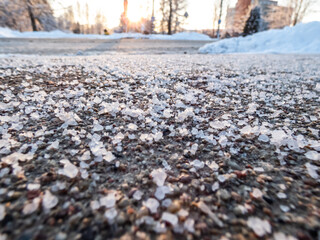 Salt grains on icy sidewalk surface in the winter. Applying salt to keep roads clear and people safe in winter weather from ice or snow