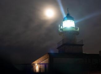 Faro en un cabo por la noche bajo la luz de la luna y las nubes 