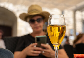 Mujer con un sombrero de paja sentada en una terraza de un bar tomándose una cerveza mientras mira...