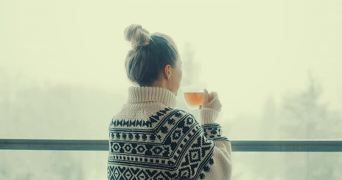 Woman drinks tea, and relax on terrace at home in winter day. Health care, authenticity, sense of balance and calmness. Fresh air, It's Snow time. 4K Video