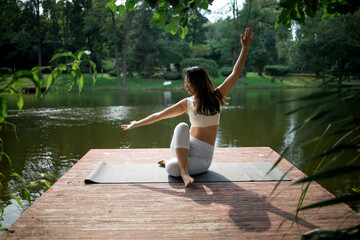 Young fit asian woman doing yoga by the lake in the morning park