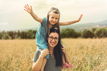 child girl with mother are playing in wheat field.