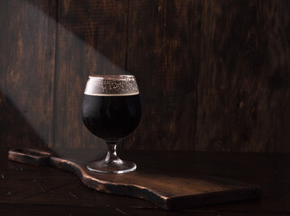 A glass of dark beer. Beer with traces of foam on the glass. Beer on the background of burnt wood.