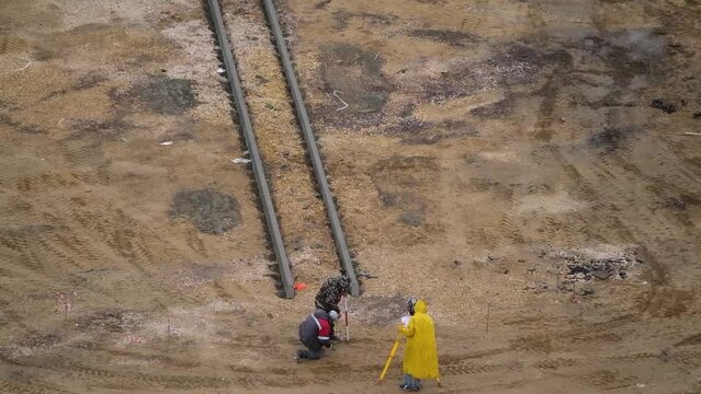 A surveyor in a yellow raincoat works at a construction site.