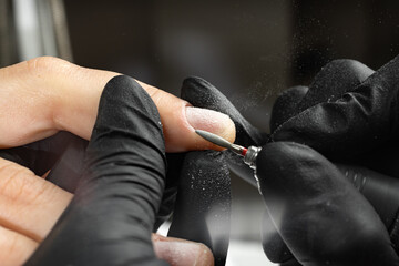 Closeup of master hands in black gloves applying an electric nail file drill to remove cuticles in the beauty salon. Perfect nails manicure process. Hardware manicure - obrazy, fototapety, plakaty