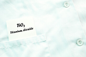 A piece of paper with TiO2 titanium dioxide written on it appears from a poket of a laboratory coat. - obrazy, fototapety, plakaty