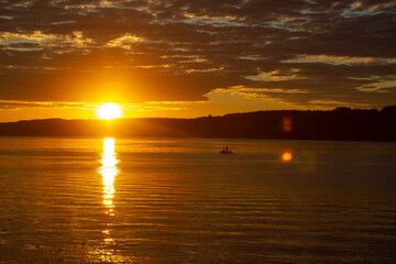 Bright sunset in the river, orange sky in dark clouds and reflection of the sun in the water