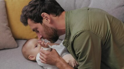 Dad plays with his little baby, on the couch in a cozy apartment. Fatherly love. Father hugs and kisses his little daughter. Paternity Leave.
