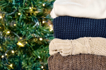 Stack of warm knitted sweaters on blurred christmas tree background. Slow Fashion. Conscious consumption. Black friday. Winter sale.