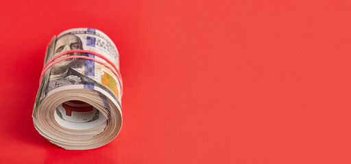 Many hundred dollar bills rolled up with a red rubber band on a red background.