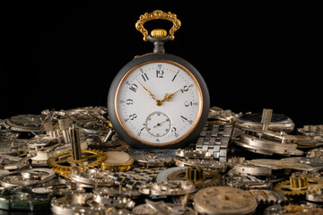 Old grey pocket watch with golden hands on pile of gears. Gearwheels, cogwheels and metal bracelet...