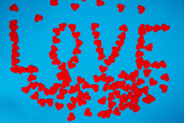Lovely pattern and word love from paper red hearts on blue screen background. Top view of heart shaped confetti. Screensaver mockup for Valentine's day, holiday, party. Symbol of love, engagement.