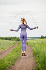 Young blonde woman doing exercises with a skipping rope on a country road - obrazy, fototapety, plakaty