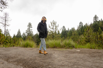 young adult woman walks through the woods while listening to music on her headphones on a gray day