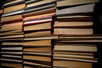 Shelves with old books. Stacks of textbooks with red, blue, green covers and paper sheets with shadow in a dark library. Stacked retro books in a bookstore.