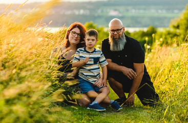 Portrait of a little boy with down syndrome in sunset on summer season with his family