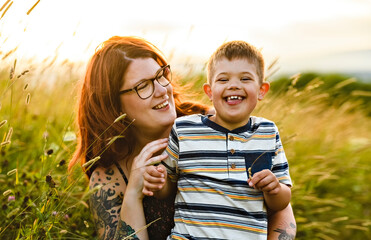 Portrait of a little boy with down syndrome in sunset on summer season with his mother