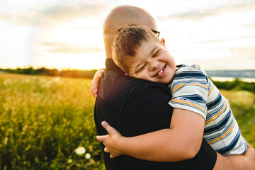 Portrait of a little boy with down syndrome in sunset on summer season with his father - obrazy, fototapety, plakaty