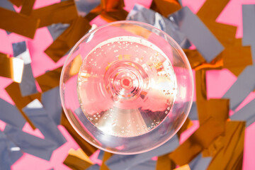 Top view of glass of sparkling champagne on a background of gold and silver tinsel. A drink with bubbles in a glass on a pink background with shiny stripes of sequins, confetti or serpentine.