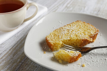 A piece of lemon cake on a plate, next to it a cup of tea.