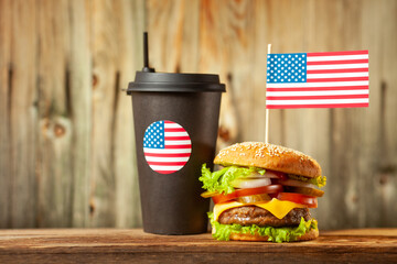 Close-up home made beef burger with american flag on the top and cup on wooden table over wooden...