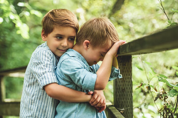 Portrait of a sad boy with down syndrome in a park with brother hug