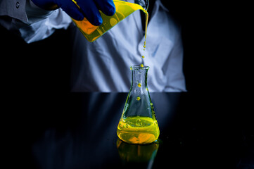 A woman scientist experimenting with a yellow fluorescent solution in a glass conical flask in dark biomedical laboratory