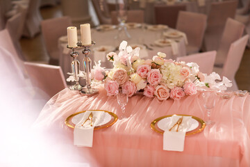 table decoration with pink tablecloth, crystal candlesticks with candles and white pink flowers in restaurant . stylish wedding day. setting table with gold plate, fork and knife