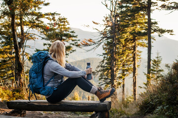 Woman resting on bench in forest. Relaxation during hiking in mountain - obrazy, fototapety, plakaty